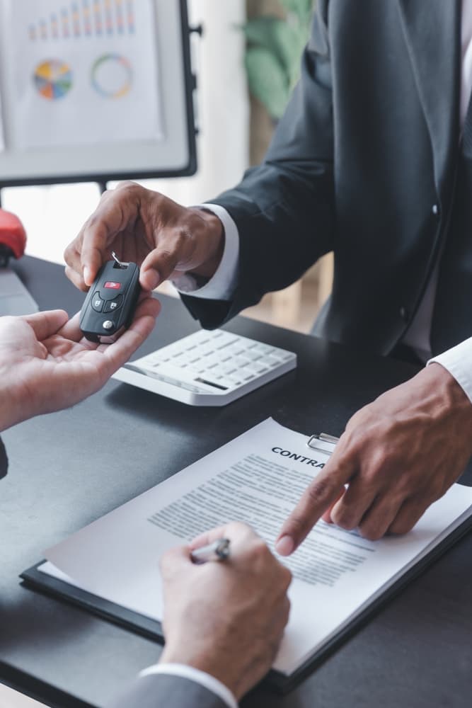 Auto insurance or rental concept: Salesman finalizing deal, handing keys to buyer after signing sales contract or rental agreement.