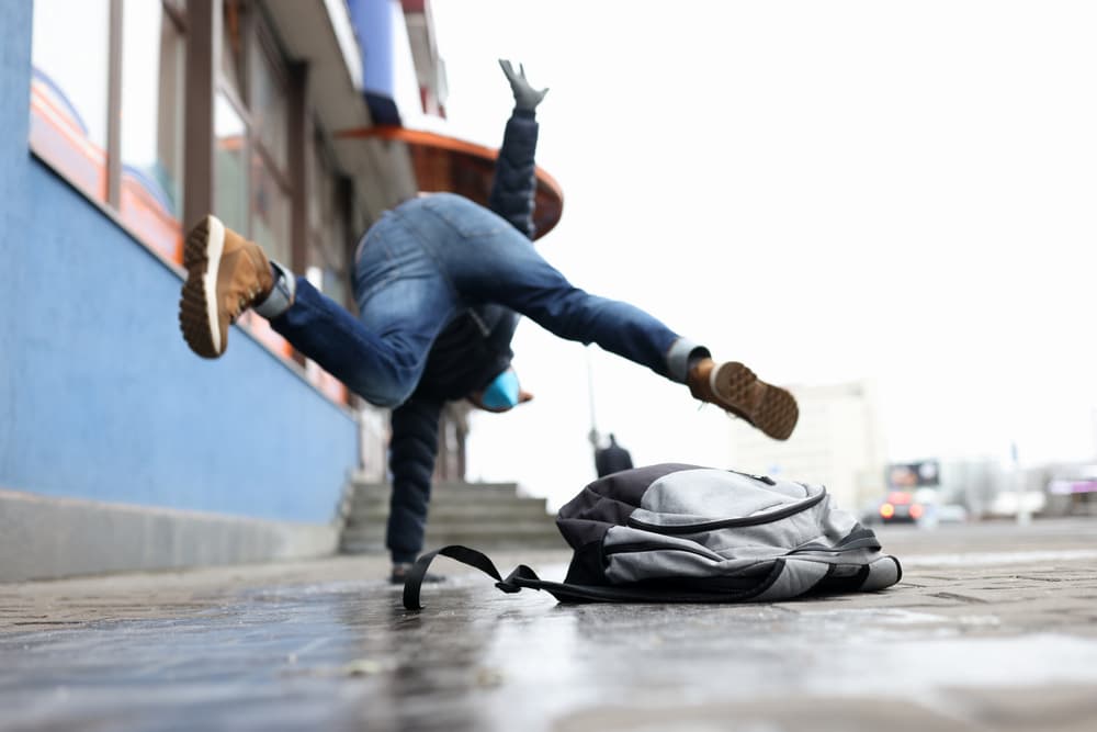 Close-up of a man in winter attire slipping on an icy sidewalk. Illustrating the importance of health insurance in unexpected situations.