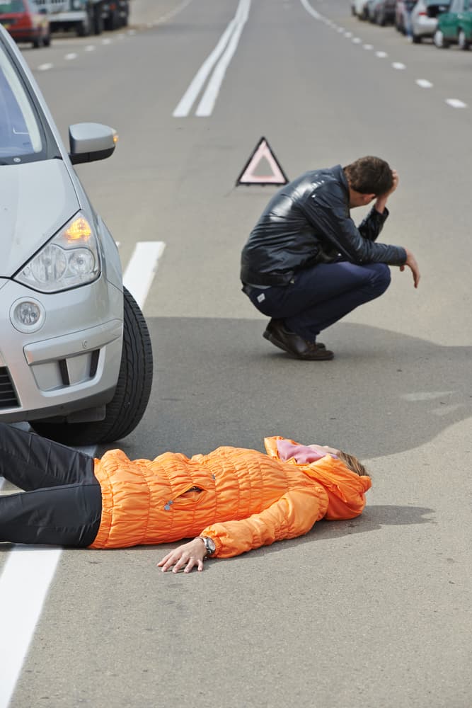Collision aftermath: A pedestrian hit on the road, distressed driver beside the crashed car. Scene of a car-pedestrian accident.