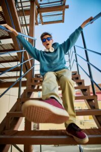 Young teenager expresses emotions while standing on metal stairs, bravely taking a step forward. Represents the resilience of the modern generation.