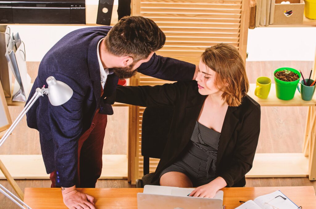 Man leaning over woman at desk, woman appears uncomfortable.