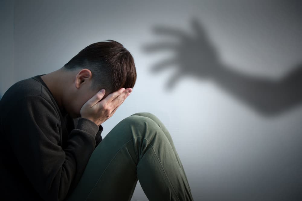 A distressed person sitting with head in hands, shadow of a hand reaching towards them.