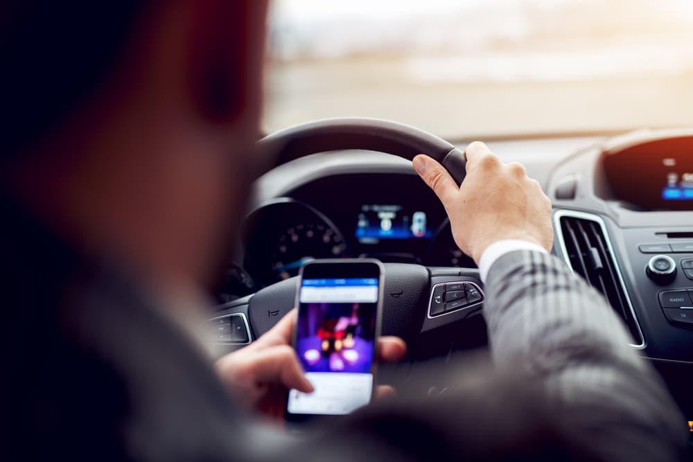 Man looking at mobile phone while driving a car.