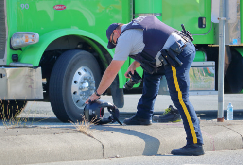 A police officer inspecting a motorcycle helmet near a green truck at the scene of an accident