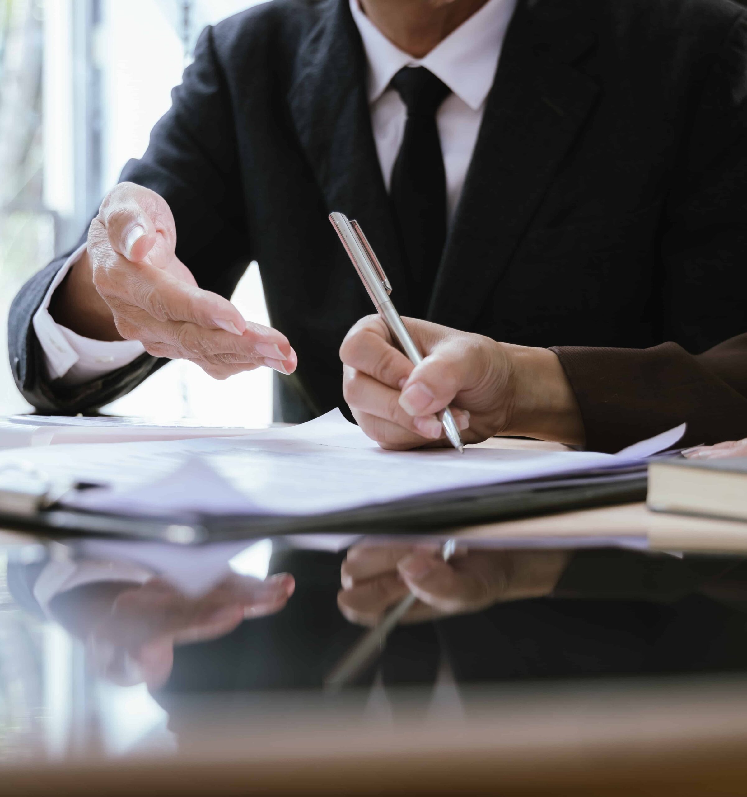Business professional signing legal documents at desk during contract or insurance agreement meeting.